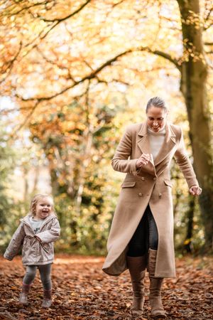 Two people play together in autumn leaves during a joyful outdoor photoshoot in a park setting.