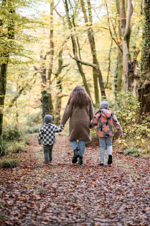 Three small children walking through a forest path covered in autumn leaves.
