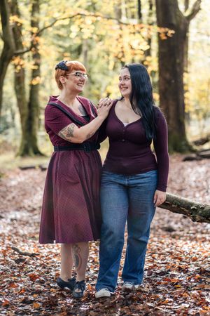 Two people share a joyful moment while standing in autumn leaves during a fall photo session in the woods.