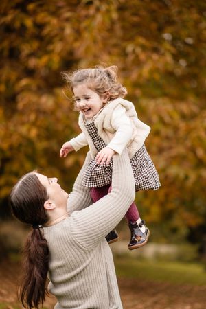 A parent and child share joyful moments together during an autumn photoshoot in a park with golden foliage.