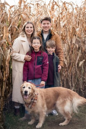 Family and their golden retriever pose together in a cornfield during a fall photoshoot.