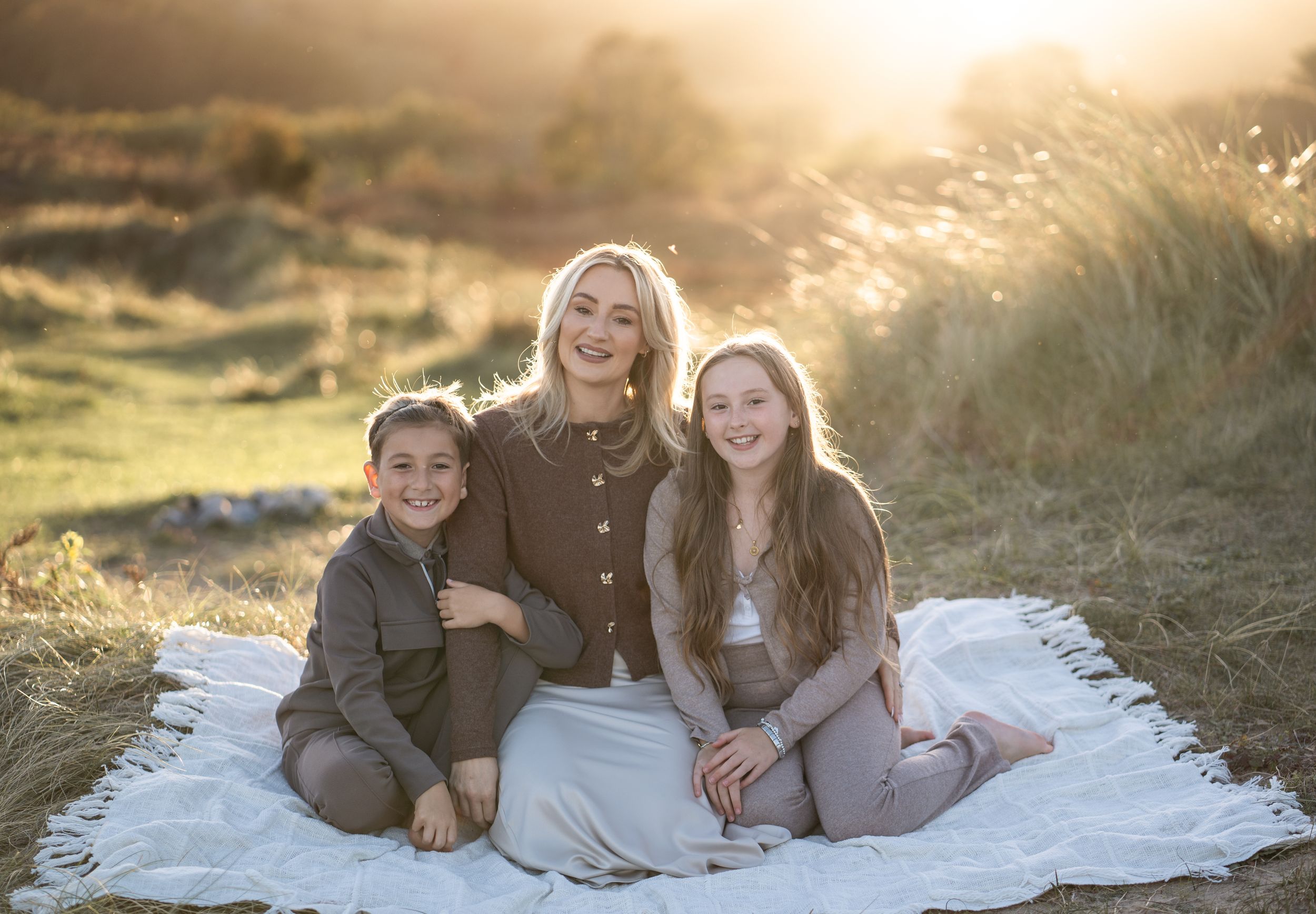 A family sits together on a white blanket outdoors during golden hour sunset photography session.