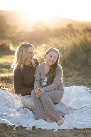 Two people share joyful laughter while relaxing on a white blanket during golden hour in a grassy setting.