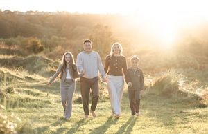 A family walks together in a golden sunlit meadow during sunset creating long shadows on the grass.