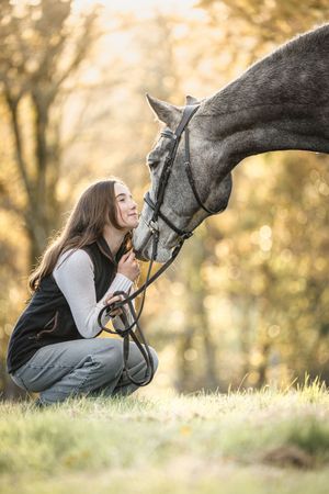 A tender moment between a person and a dark horse touching noses in an autumn forest setting.