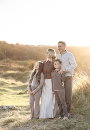 A family of four poses together on a grassy hillside during golden hour.