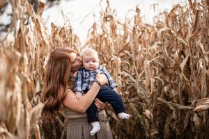 A parent and child share a tender moment among tall dried corn stalks in an autumn field.