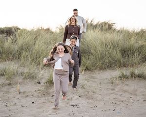 A joyful family runs and plays together through coastal sand dunes on a sunny afternoon.