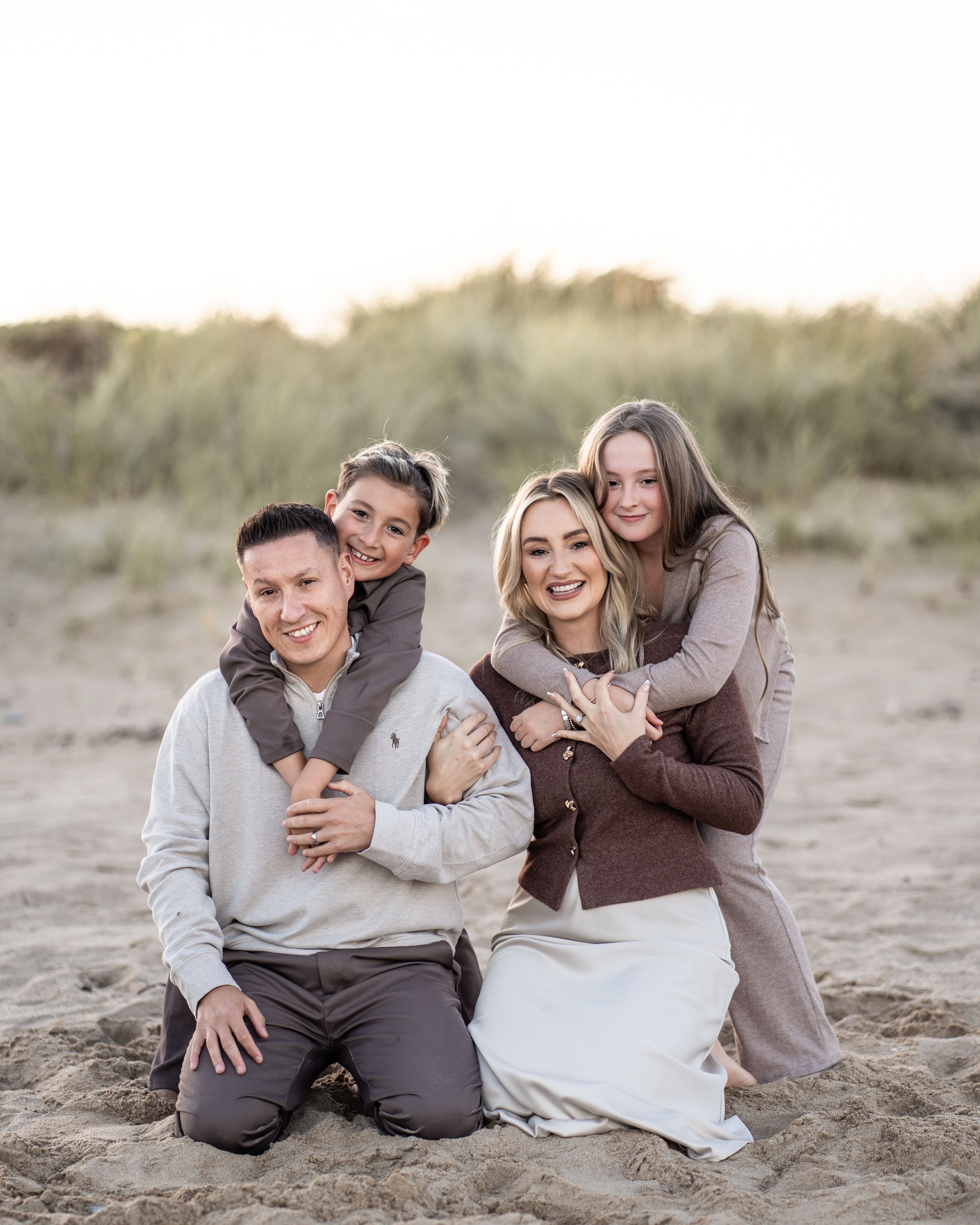 A loving family poses together on sandy beach dunes during a sunset photoshoot.