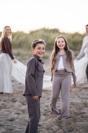 A series of candid beach photos showing people in gray and white outfits playing and laughing together on sandy dunes.