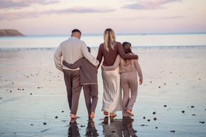 Three people walking together on a beach during sunset with their backs to the camera.