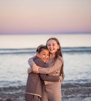 People embracing and laughing together while standing in shallow ocean water during sunset.