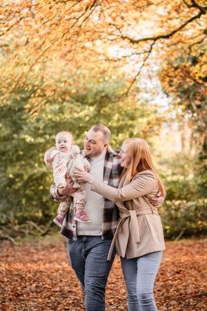 A family enjoys a tender moment together in a park filled with golden autumn leaves.