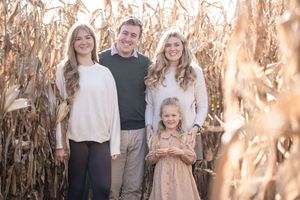 Family group poses together in autumn cornfield with golden sunlight filtering through dried stalks.