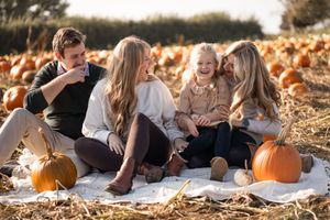 Family photo session at a pumpkin patch with warm autumn lighting and scattered orange pumpkins.