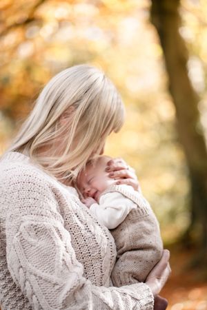 Person in cozy white knit sweater embraces a baby against warm autumn background with golden bokeh lighting.