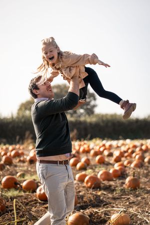 A playful moment captured at a pumpkin patch as a child is lifted high in the air.