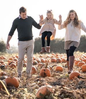 Group enjoying a fun autumn day at a pumpkin patch with orange pumpkins scattered across a sunny field.