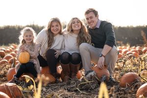 Family enjoying autumn activities in a pumpkin patch during golden hour sunset.