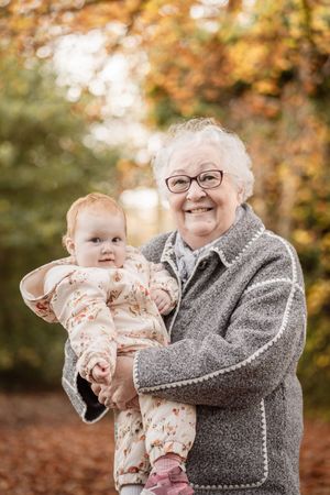 A heartwarming autumn scene with a baby and adult sharing joyful moments among orange and brown fall foliage.
