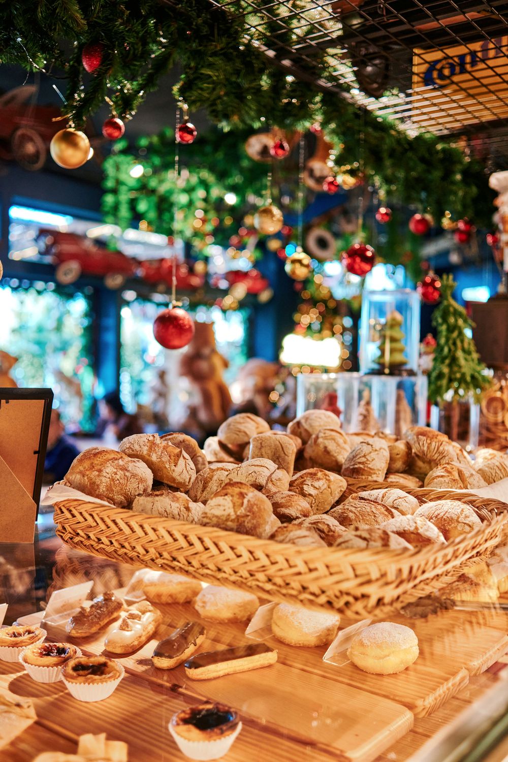 Artisan bread rolls displayed in a wicker basket at a Christmas-decorated bakery counter with festive ornaments.