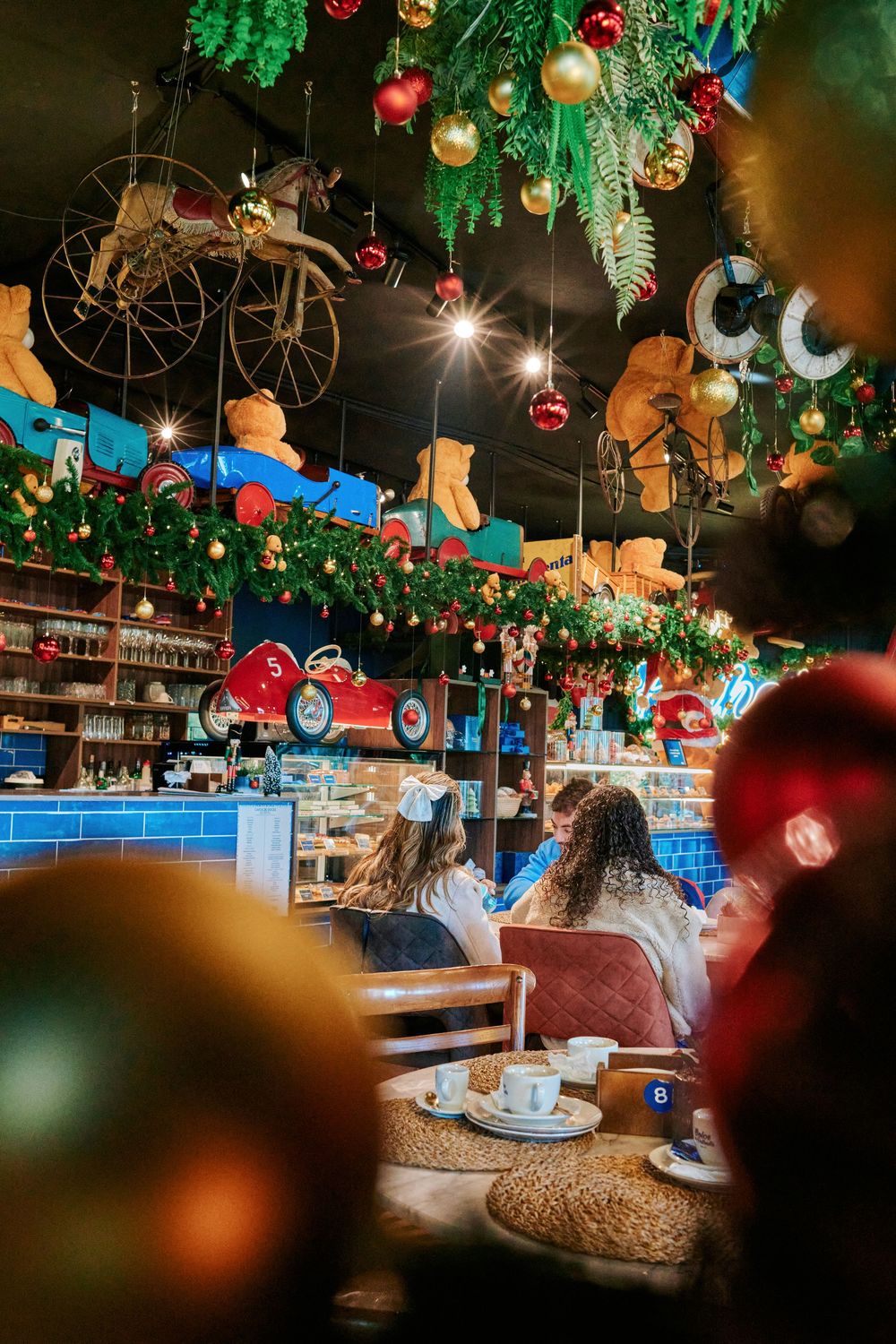 Festive cafe interior decorated with vintage toys, teddy bears, and Christmas ornaments on the ceiling.