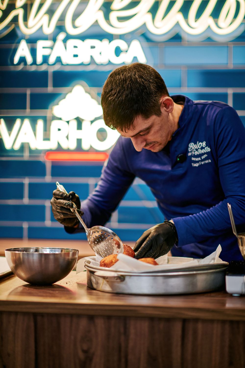 Professional chef in blue uniform carefully plating desserts at a Valrhona chocolate factory event.