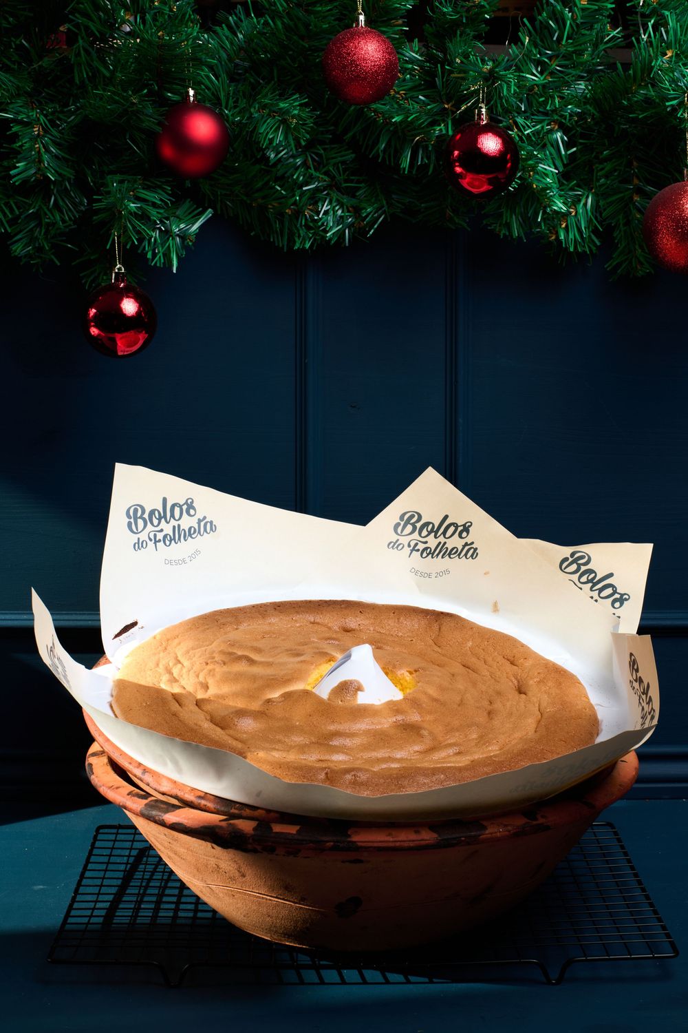 Traditional Portuguese Bolo de Folheta cake in a clay bowl under Christmas tree decorations.
