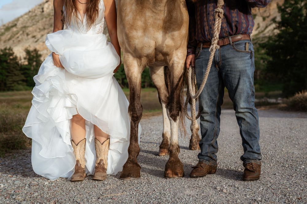 Chest down shot of bride, groom, and horse facing camera and displaying their cowboy boots and horse shoes.