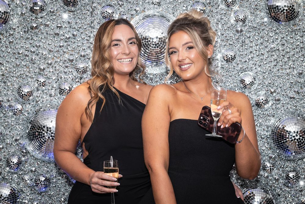 Friends posing together at a glamorous party with sparkly silver backdrop and champagne glasses.