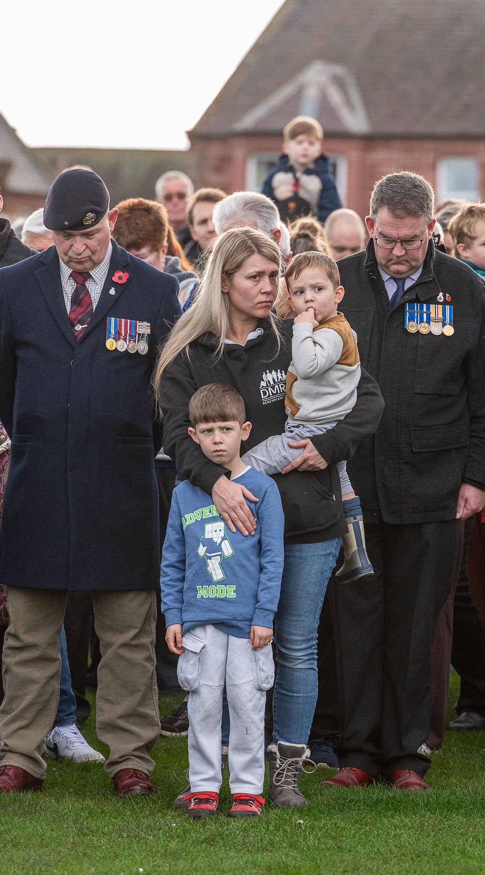 A young child stands among a crowd of veterans and attendees during an outdoor remembrance ceremony.