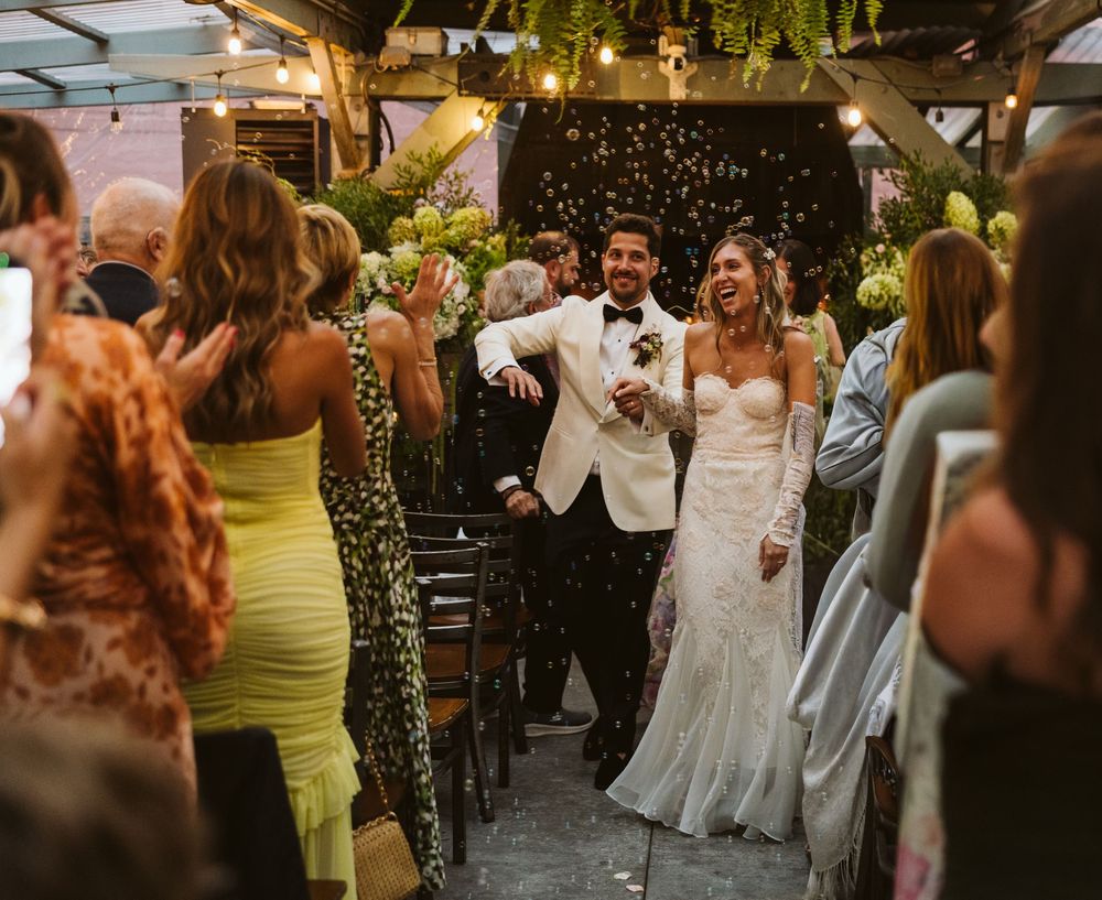 Wedding celebration at an outdoor venue with guests dancing and celebrating under twinkling lights and greenery.