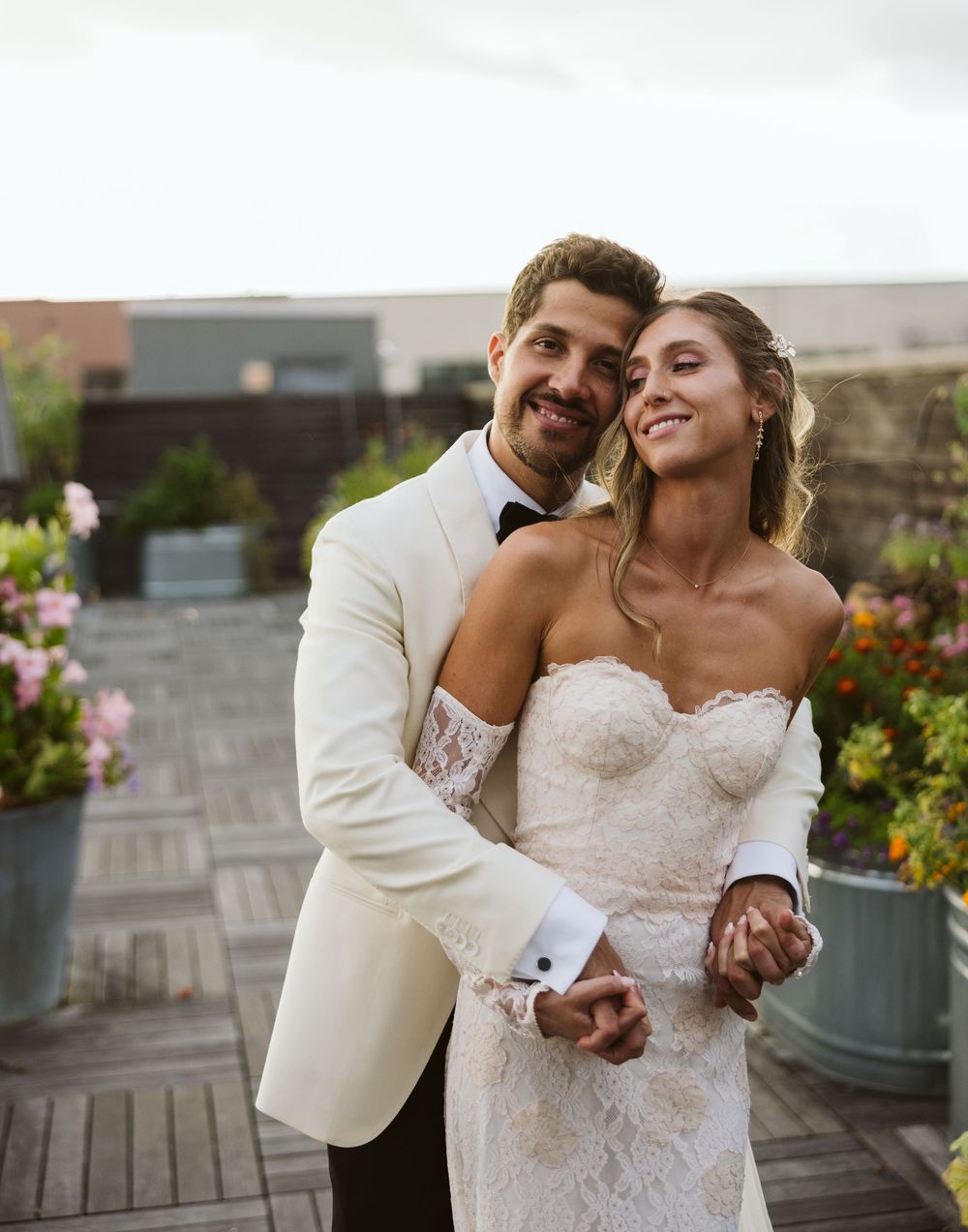 Happy couple sharing a joyful moment together on a rooftop terrace with flowers in the background.
