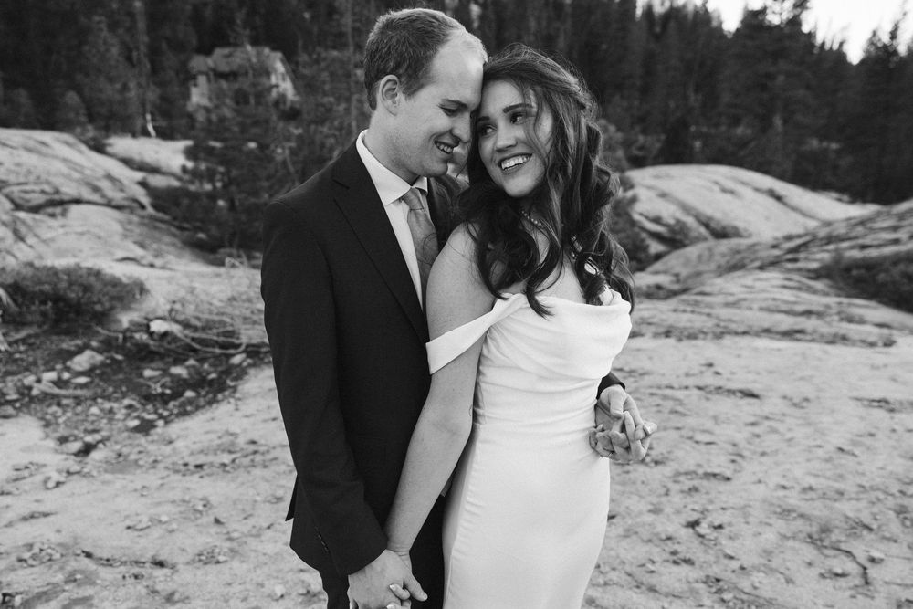 A black and white wedding photo of a couple embracing on a rocky outdoor landscape.