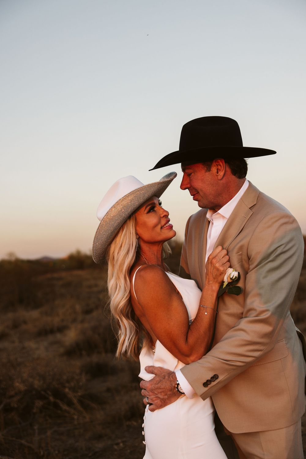 A couple in western attire shares an intimate moment during their desert wedding.