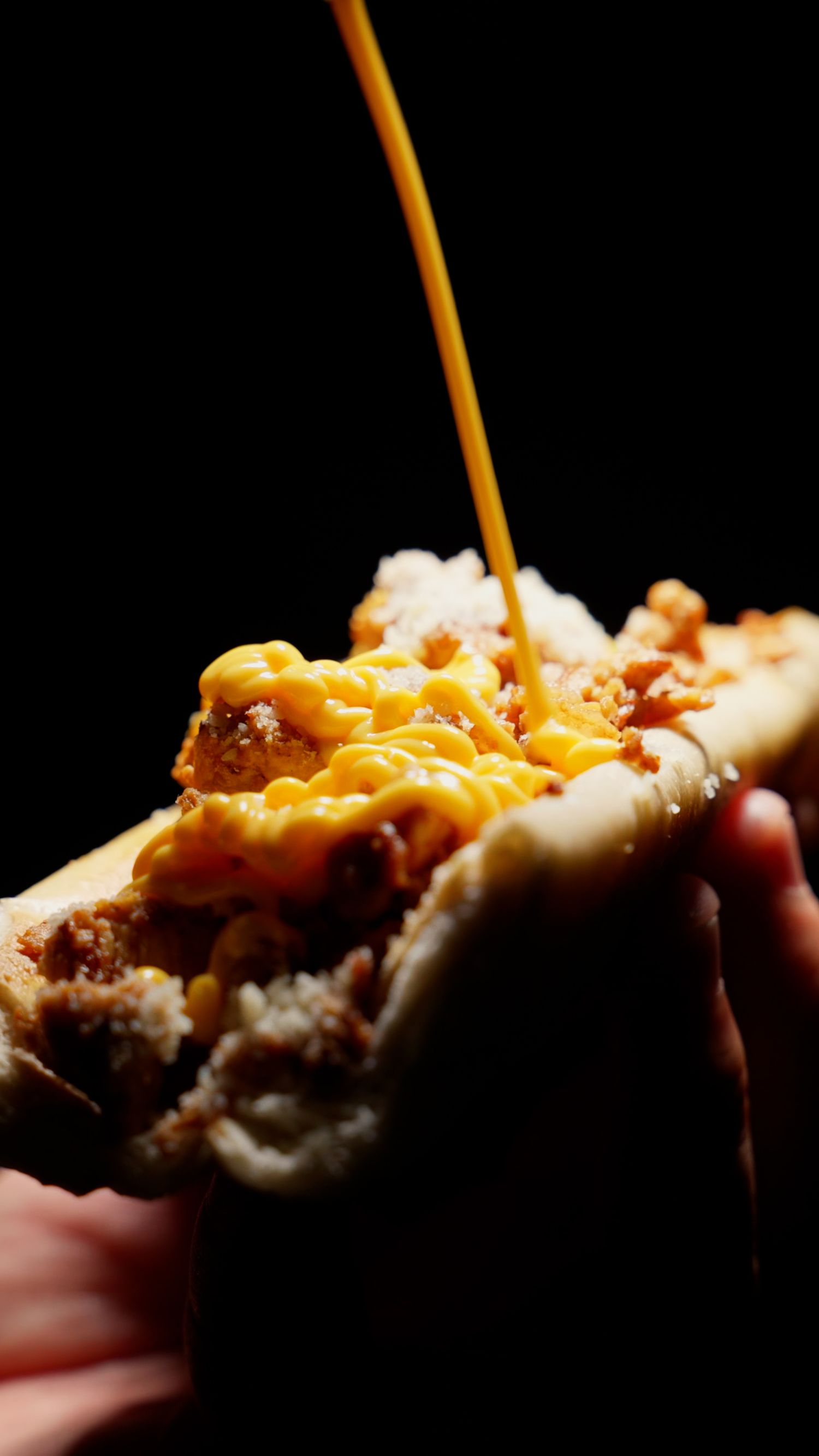 Melted yellow cheese sauce being drizzled onto a burger against a black background.