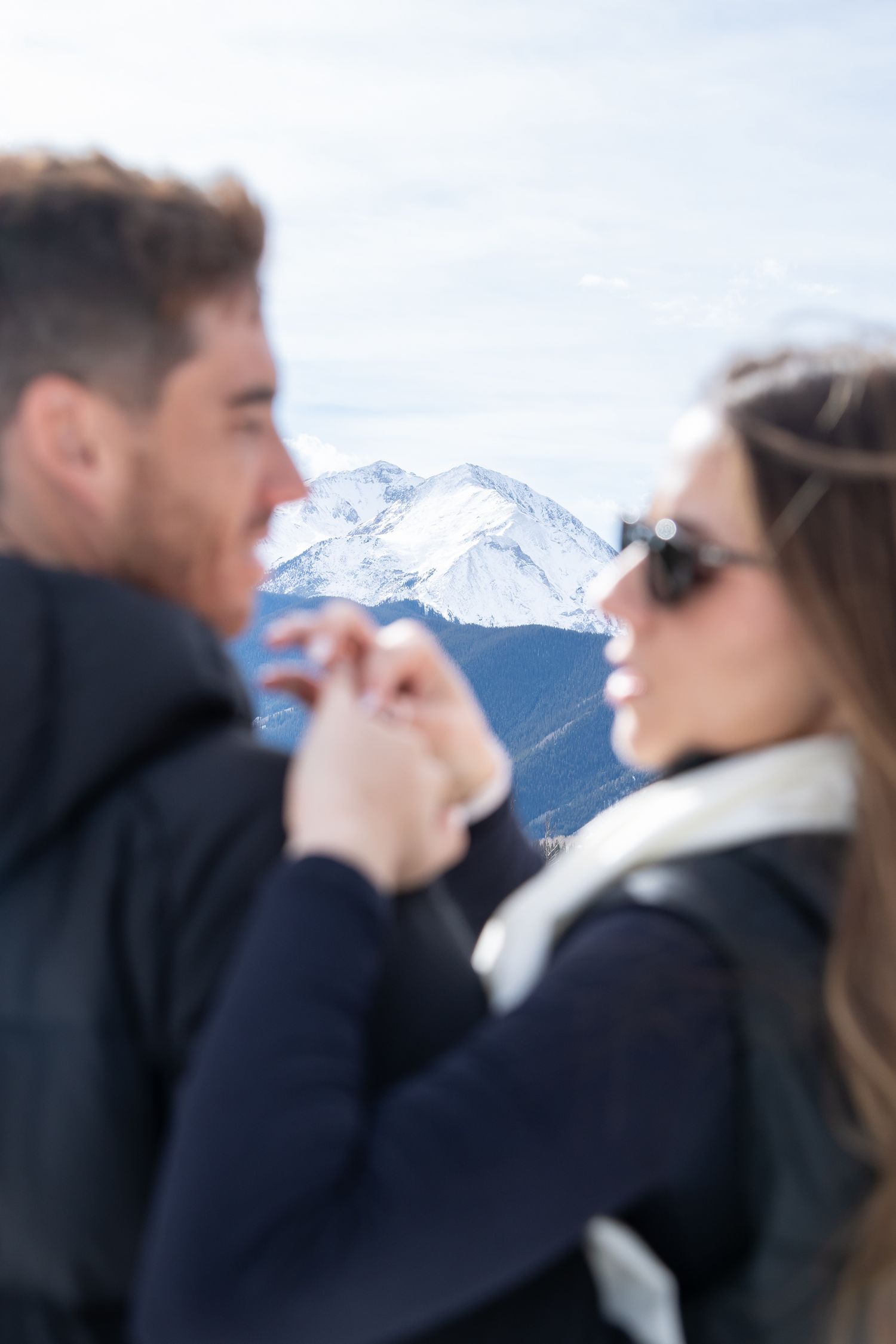 Editorial image of a mountain peak with a couple in the foreground, the woman admiring her new engagement ring after Aspen engagement.