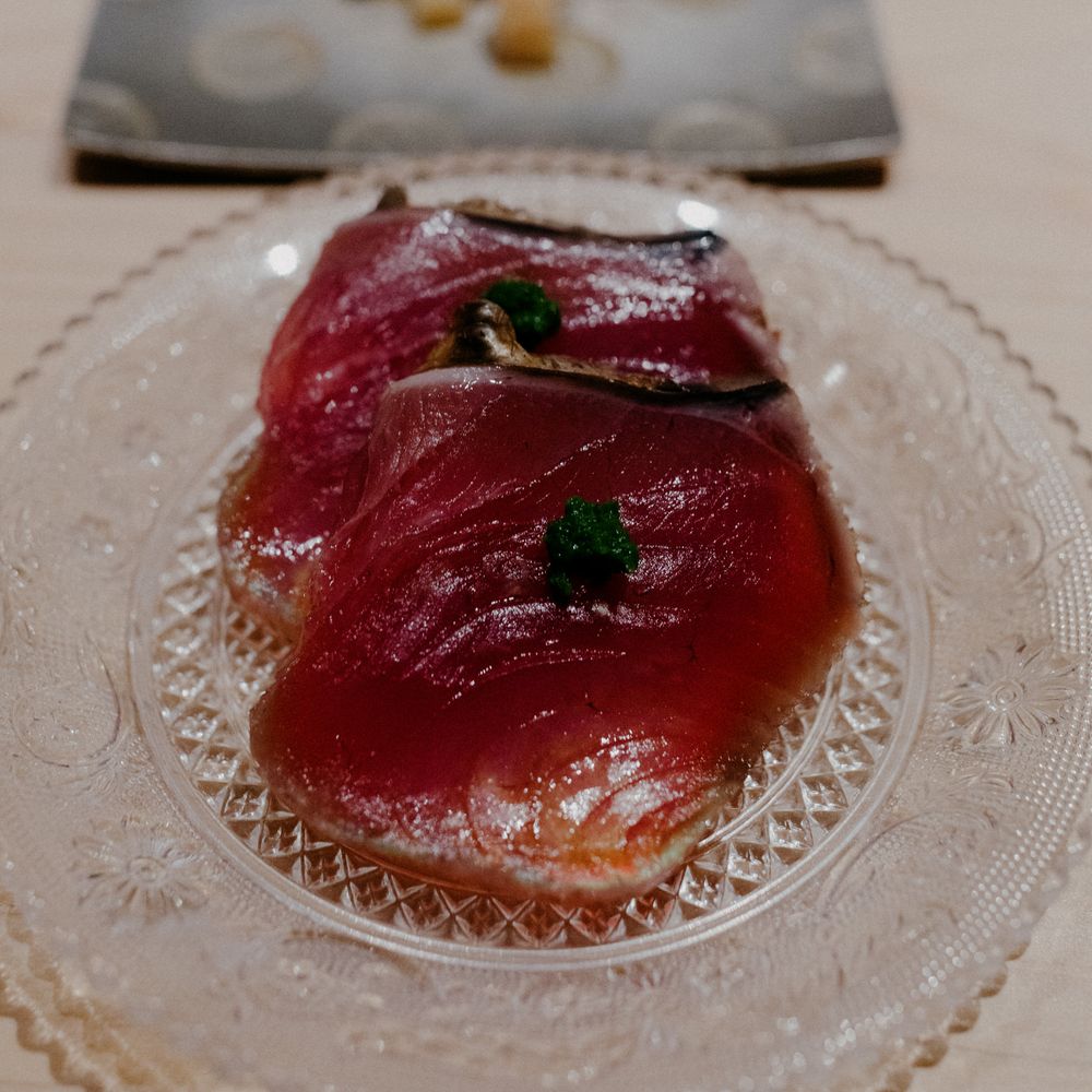 Vibrant red tuna sashimi with microgreens on crystal serving plate.