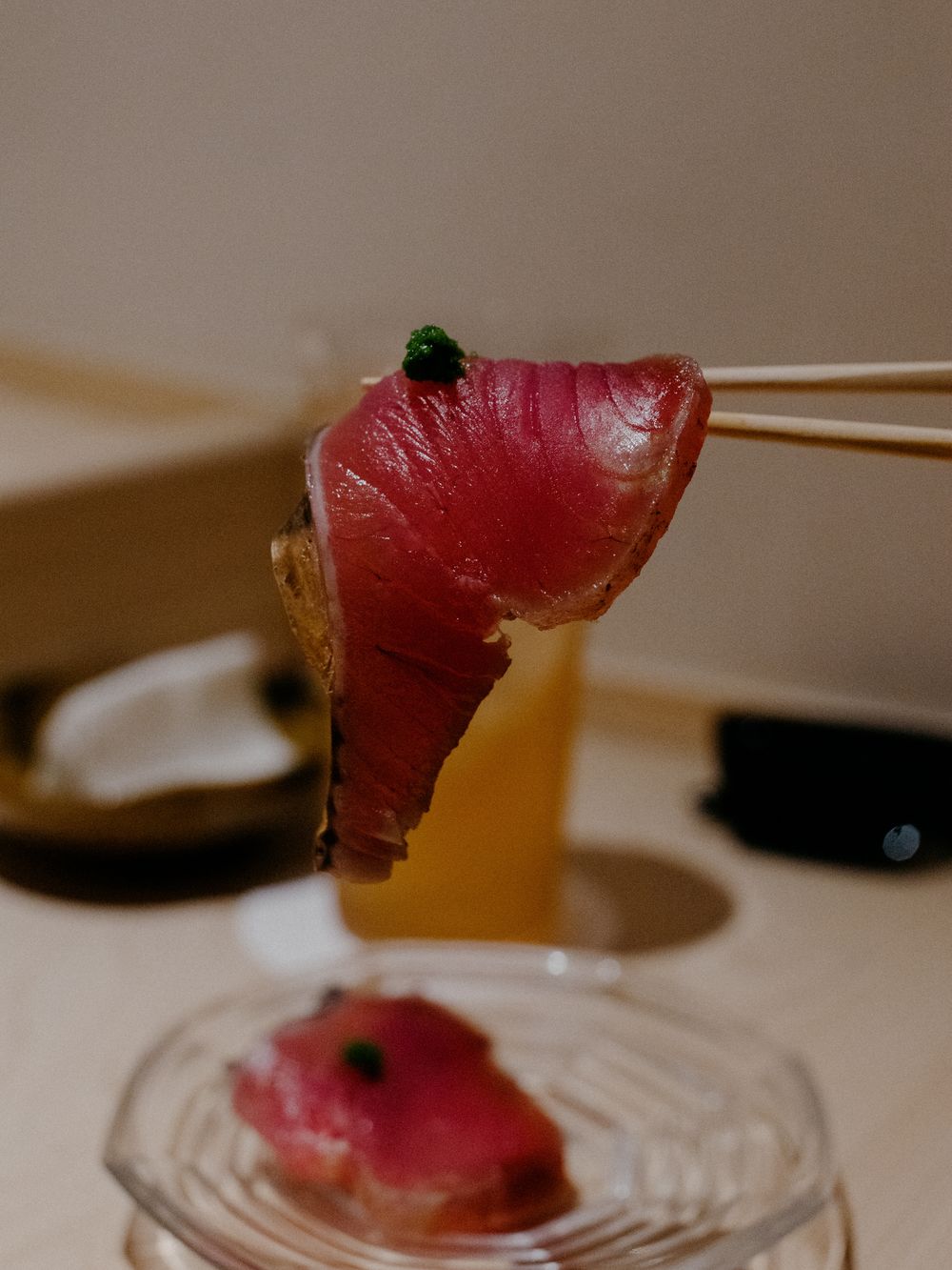 Fresh tuna sashimi slice held by chopsticks over a glass plate with garnish.