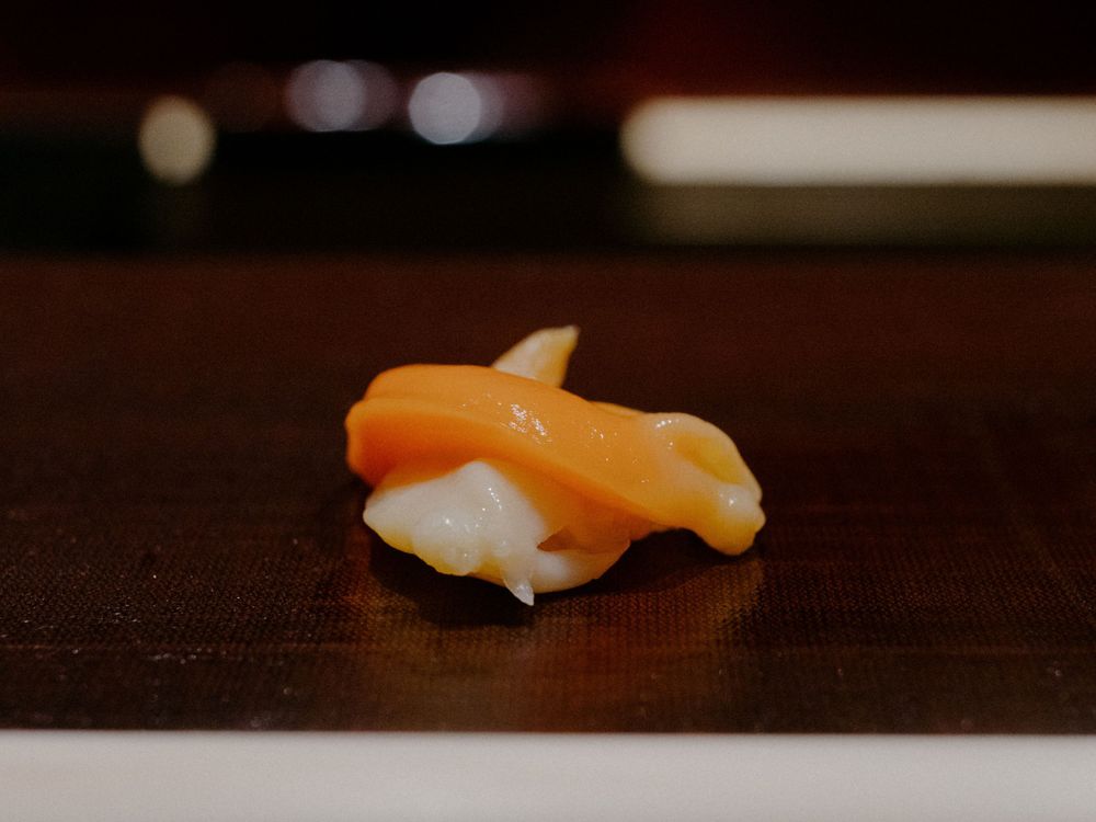 Close-up of a salmon nigiri sushi piece on a dark surface.