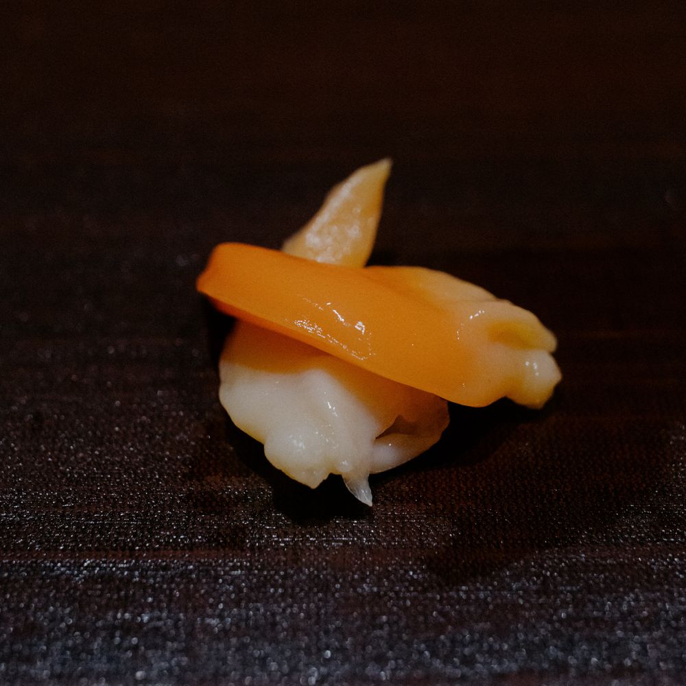 Artfully plated salmon nigiri sushi with fish draped over rice on dark background.