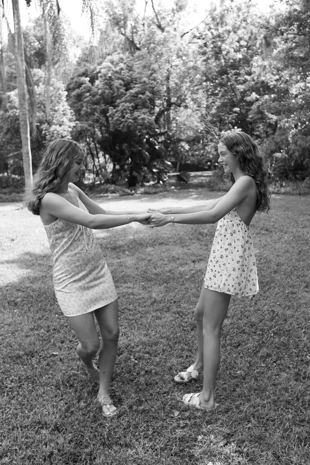 Black and white photo of two girls in summer dresses holding hands and spinning together on a grassy lawn.