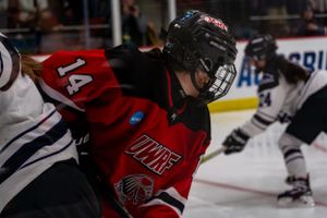 A hockey player in a red and black jersey number 14 leans forward during a face-off at a game.