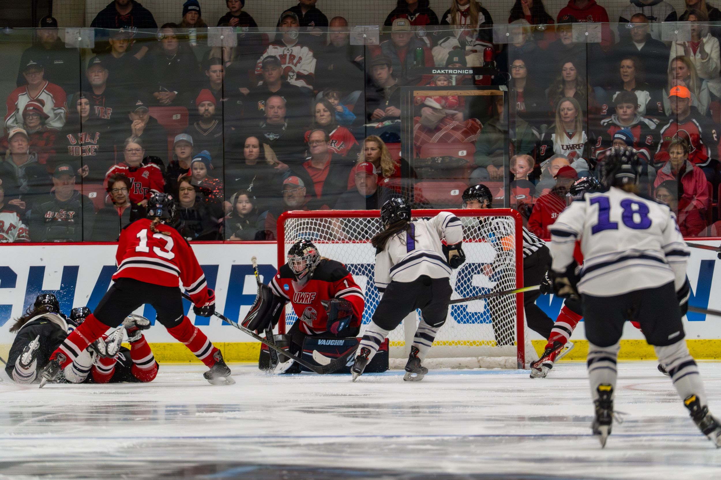 Hockey players scramble for the puck in front of the net during an intense game action sequence.