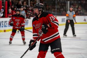 Ice hockey player in red and black jersey number 15 positions for the puck during competitive game.