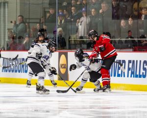 Hockey players in black and red jerseys battle for the puck during an intense game on the ice.