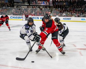 Hockey players in red and black jerseys battle for puck control during an intense ice hockey game.