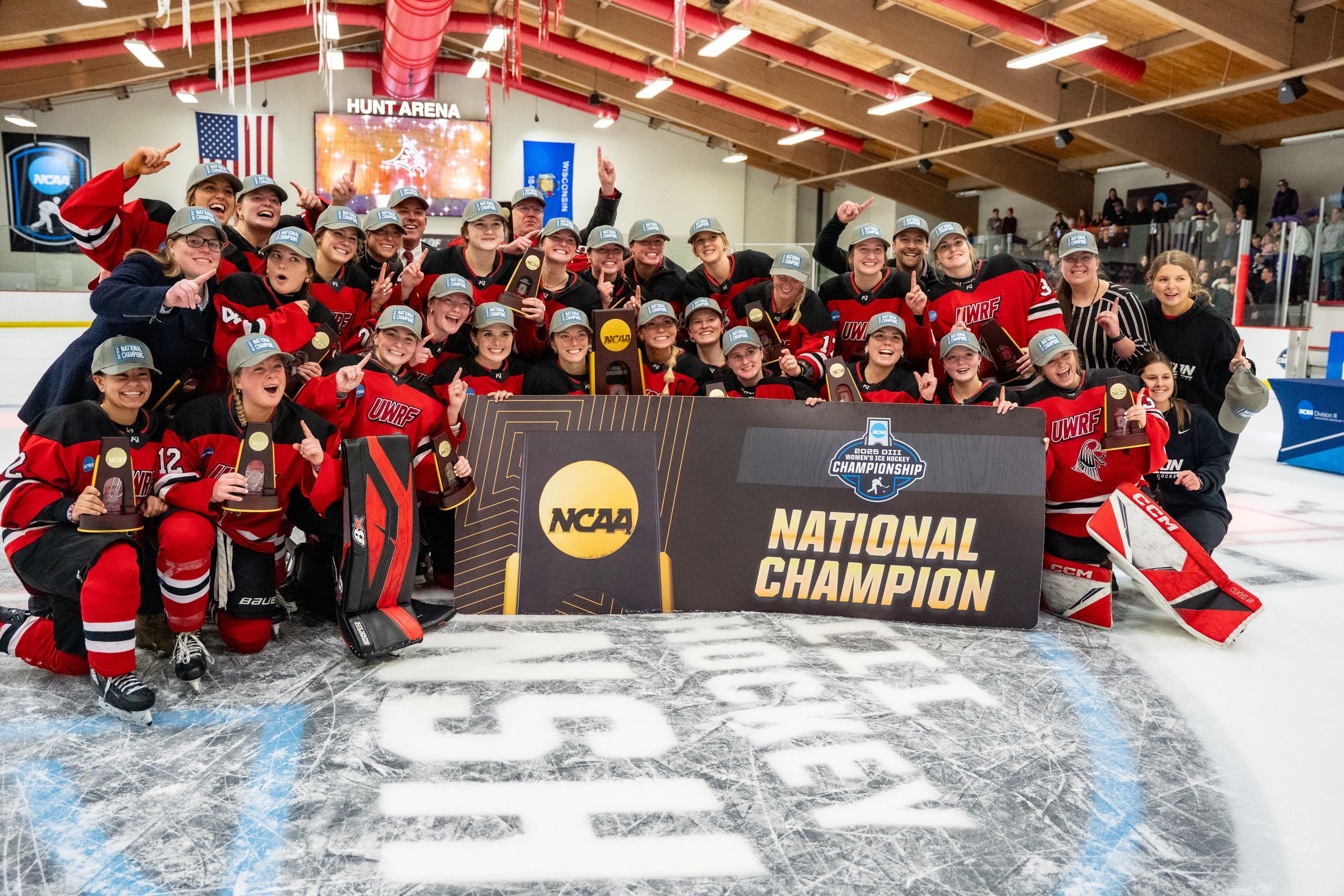 Hockey team celebrates on ice with NCAA National Championship banner and trophy after winning championship game.