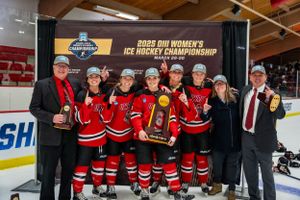 Hockey players in red jerseys pose with trophies and officials at an ice hockey championship event.