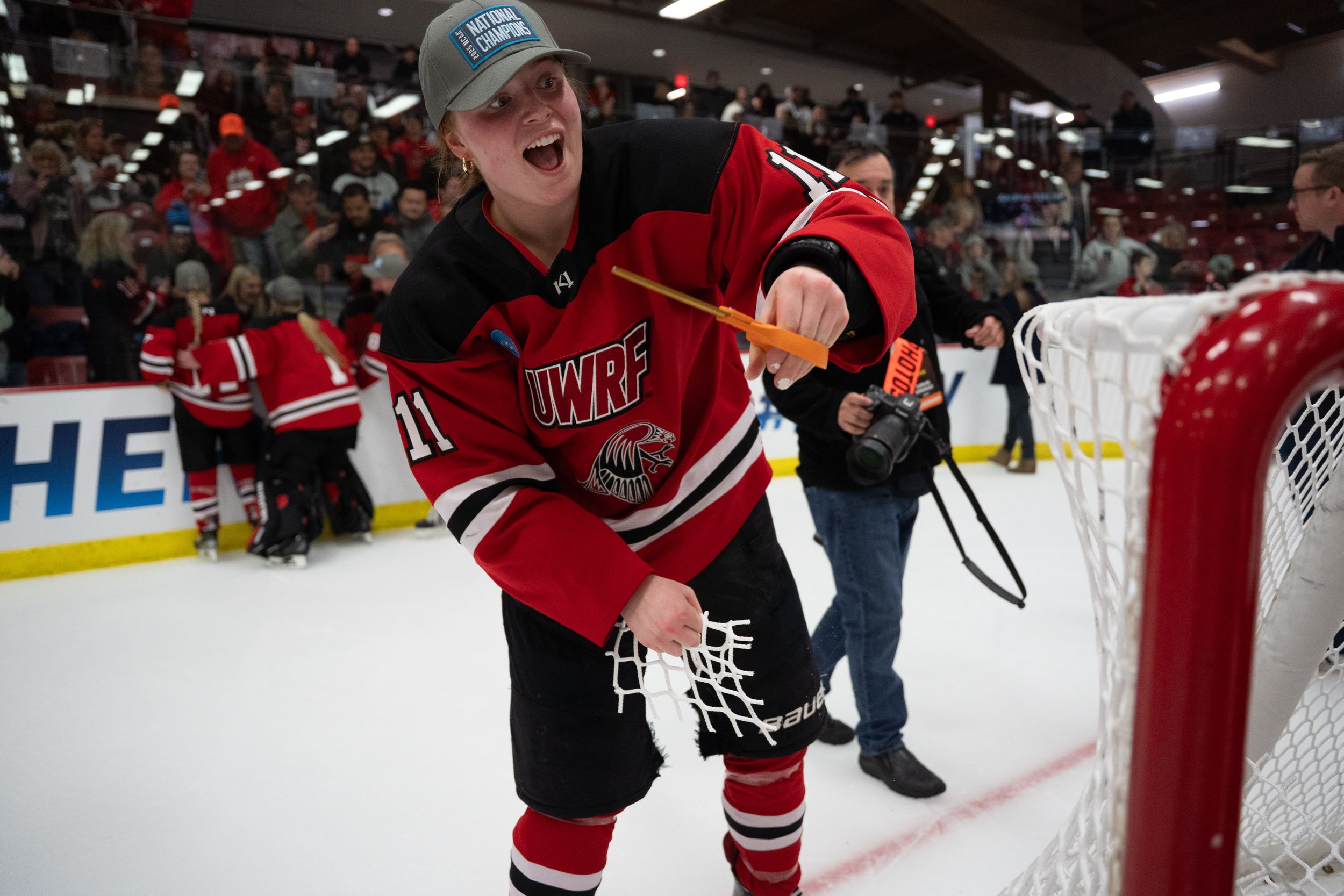 An enthusiastic youth hockey player leaning over the boards towards the ice surface during a game at an indoor rink.